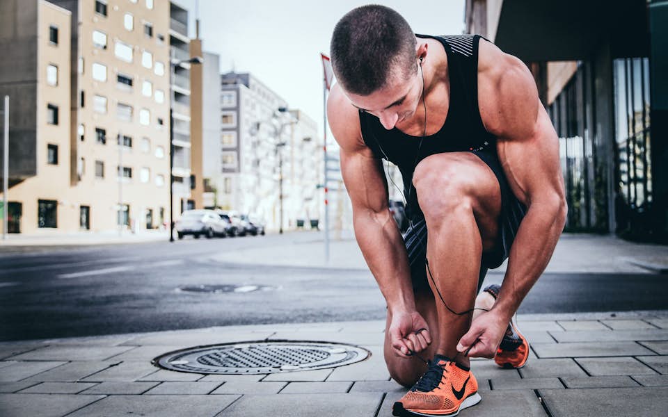 Male athlete lacing up his tennis shoes to prepare for a run in the city.