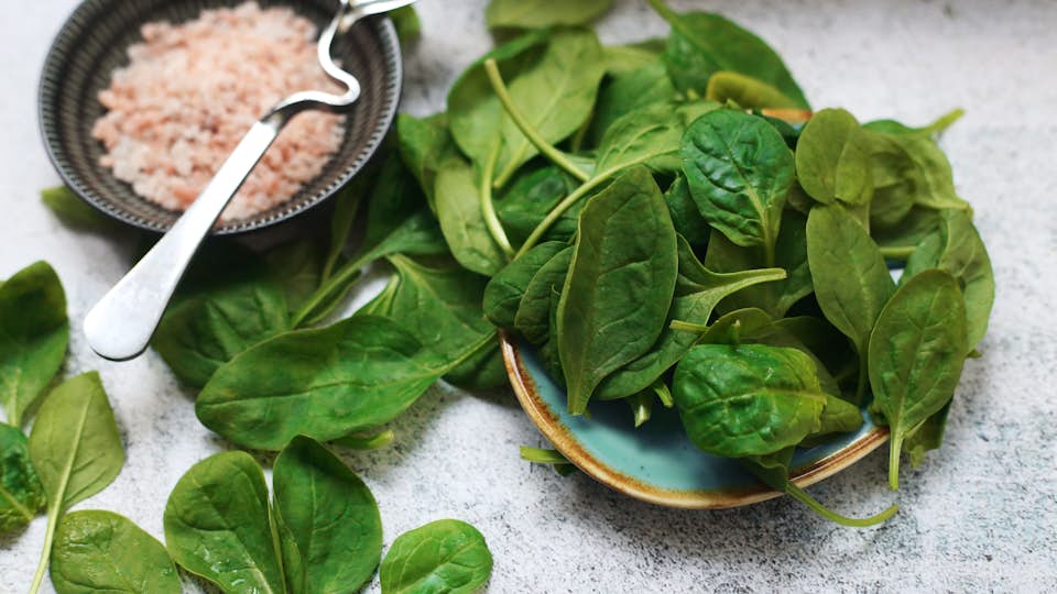 Folate-rich spinach and leafy greens in a blue ceramic bowl.