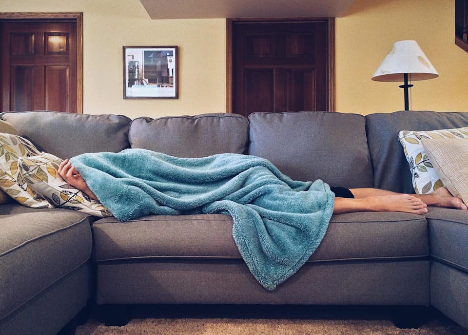 Hungover woman lying on the couch with a fuzzy blue blanket.