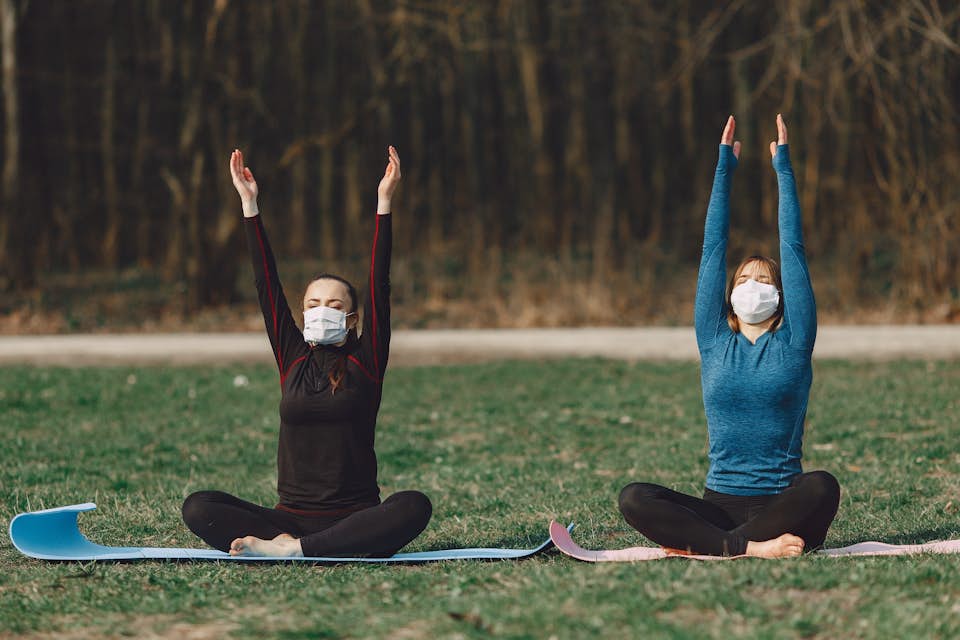 two women wearing masks detoxify with yoga in the park