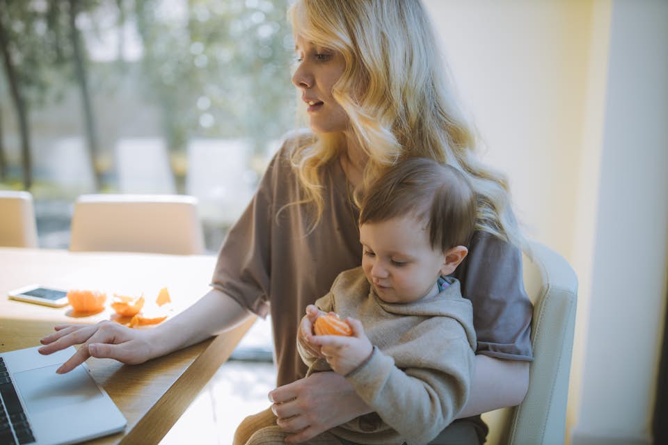 Woman working from home with baby eating a vitamin c orange